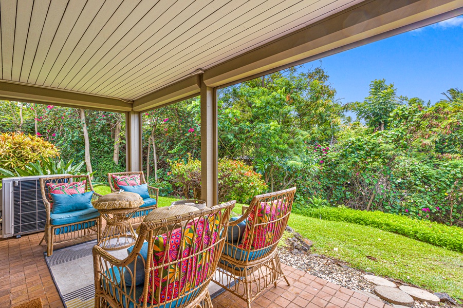 Relax on the covered lanai, surrounded by lush greenery and comfortable seating, perfect for enjoying the outdoors.