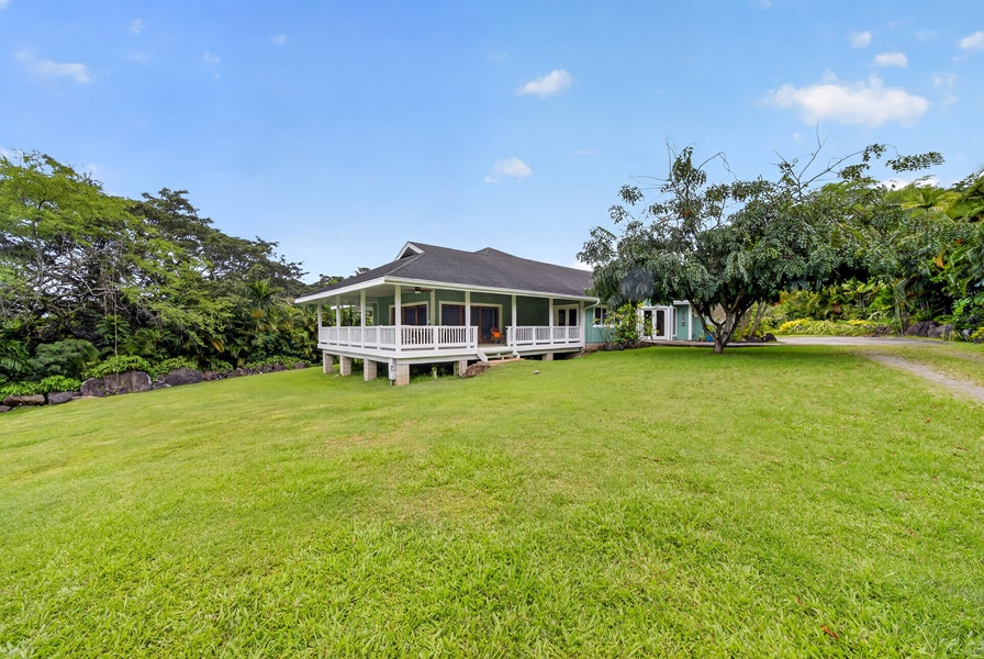 Charming plantation-style home set on manicured grounds, surrounded by lush tropical greenery and mature trees.