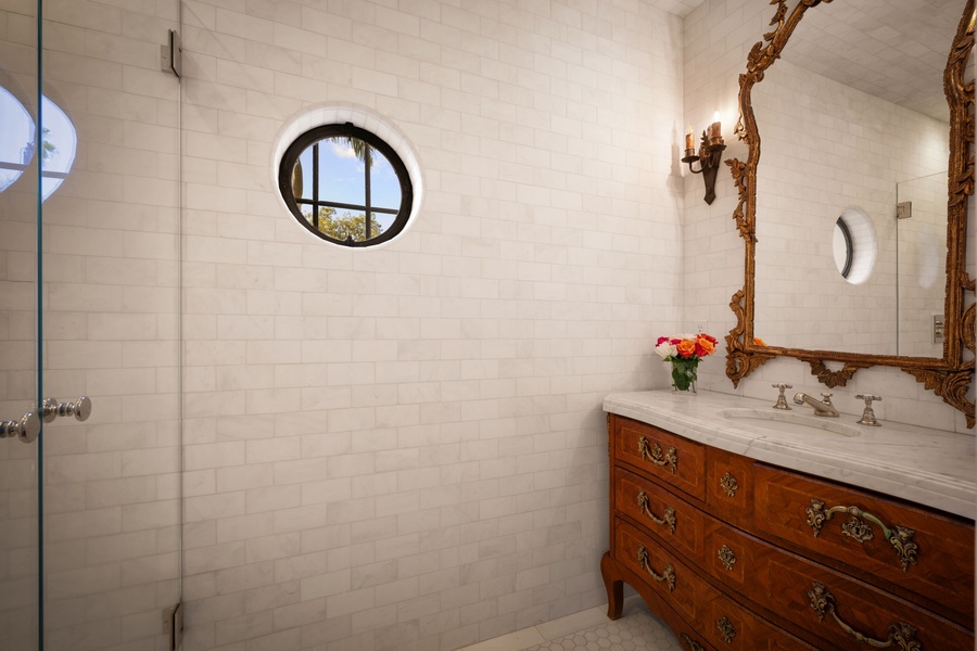 Refresh in your elegant bathroom with marble surfaces, ornate mirror, and charming round window bringing in natural light.