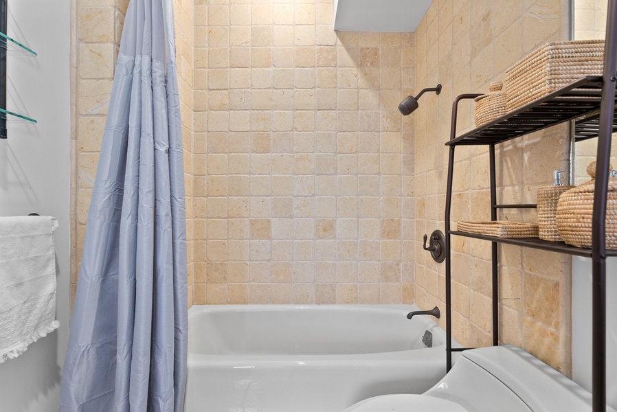 Natural stone tile and warm finishes lend this guest bath an inviting, spa-like feel.