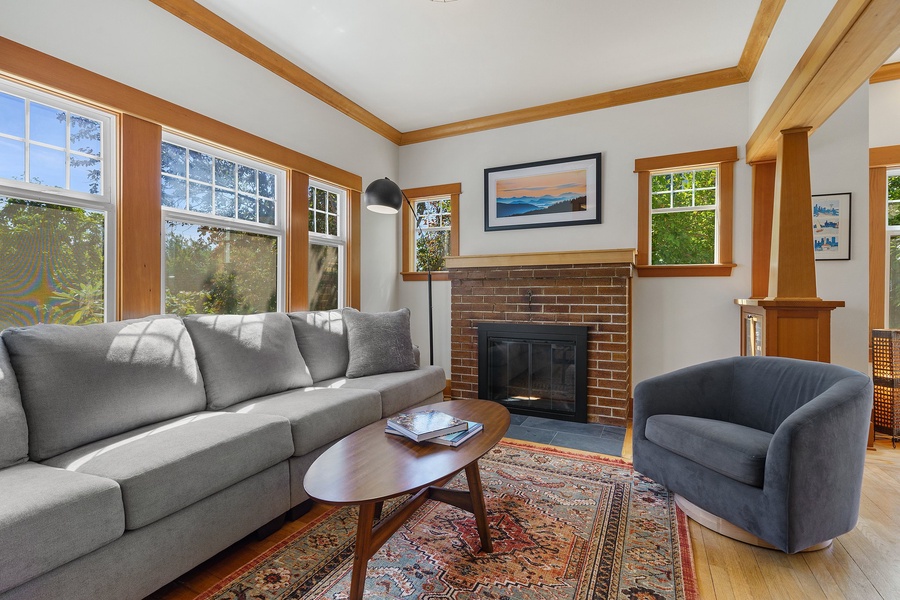 Bask in the warmth of the living area, where natural light floods through the window pane, illuminating the cozy sectional sofa by the fireplace.