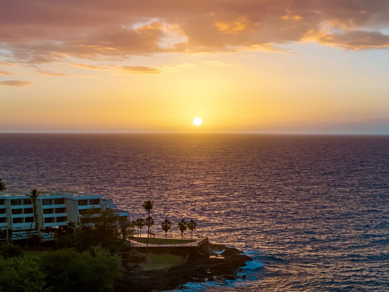 Golden sunset paints the sky above oceanfront property with dramatic clouds and shimmering waters stretching to the horizon.