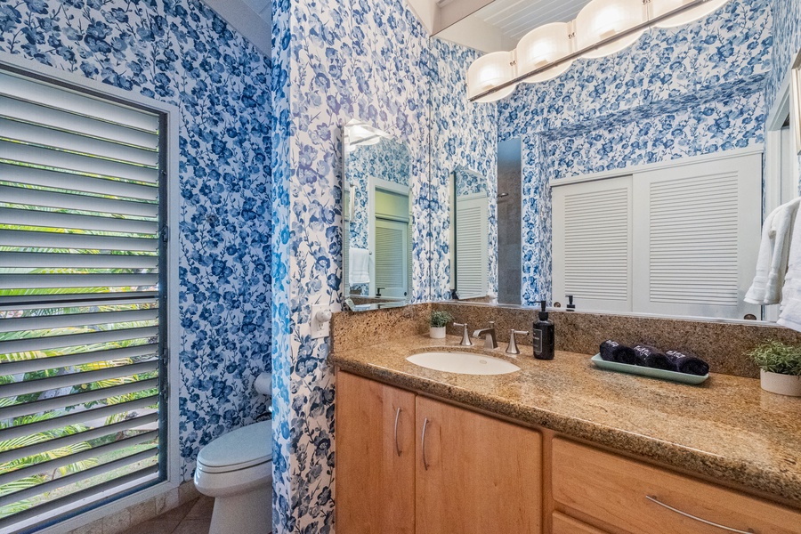 This bathroom features a large countertop, stylish wallpaper, and natural light for a refreshing space to start or end your day.