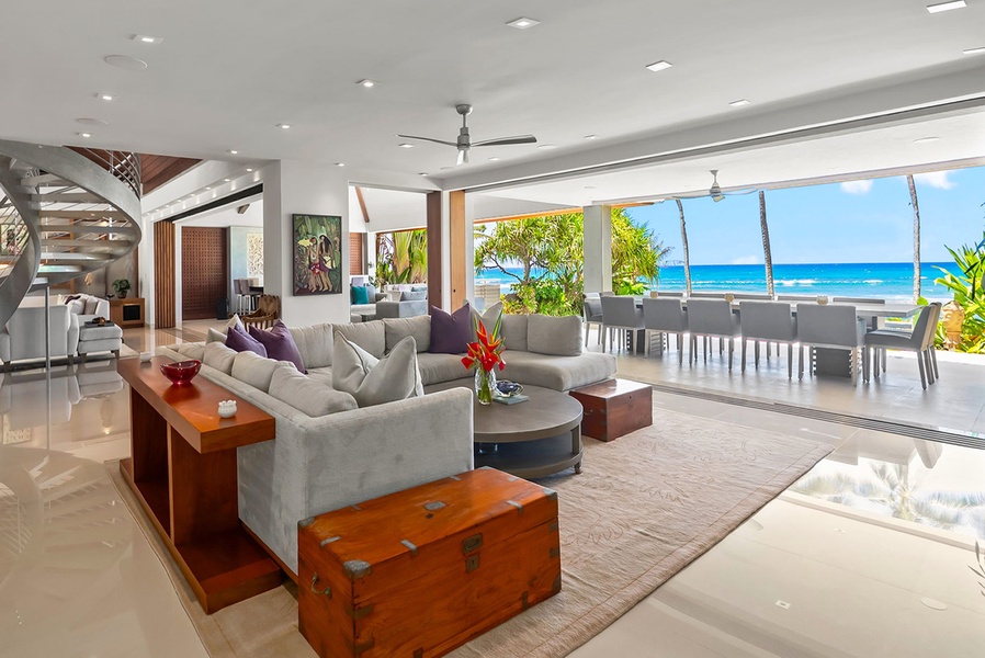 Sink into plush comfort in this elegant living space where ocean breezes flow through open walls, framing your private beachfront paradise steps away.