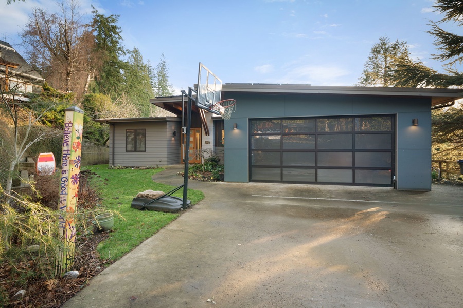Modern property featuring a glass garage door, outdoor basketball court, and landscaped grounds in a quiet residential setting.