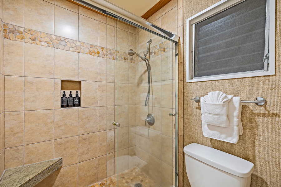The bathroom at Kahana Sunset B4B boasts a tiled walk-in shower with a glass door and built-in shampoo niche for a spa-like experience.