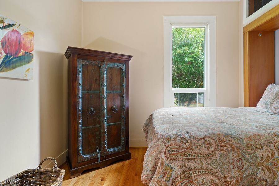 Sink into this cozy bedroom where natural light filters through your window, highlighting beautiful hardwood floors and vintage charm.