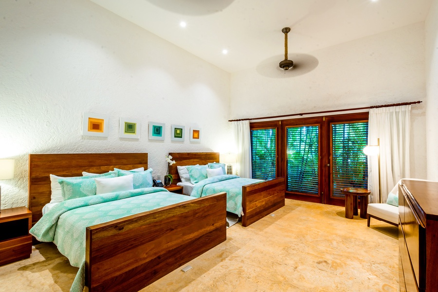Cozy guest bedroom features two queen beds and a view of lush greenery.