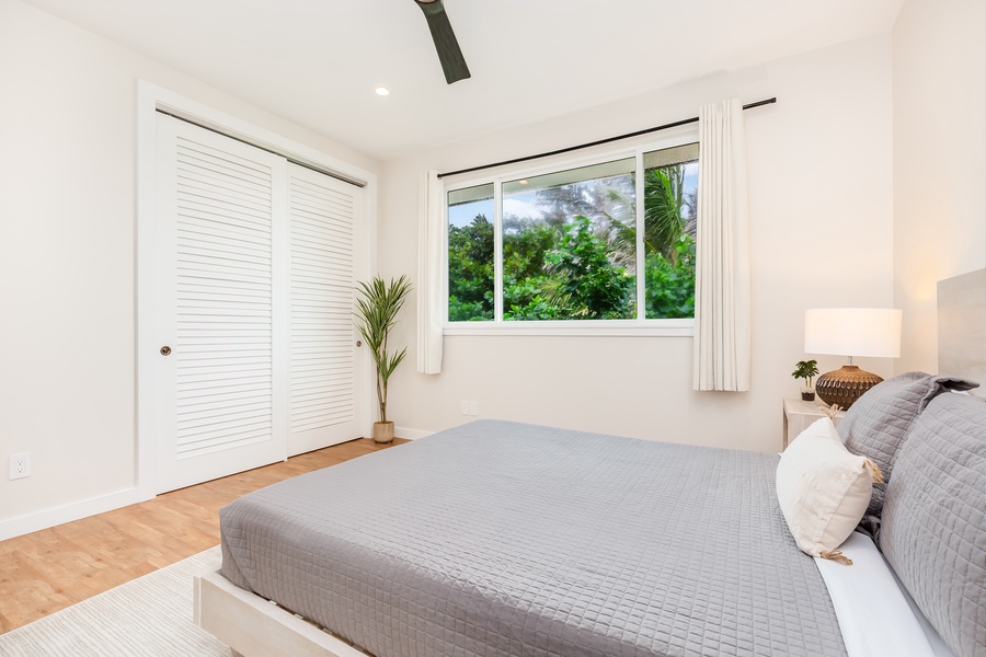 Cozy second guest bedroom with minimalist decor and lush greenery visible through the windows.