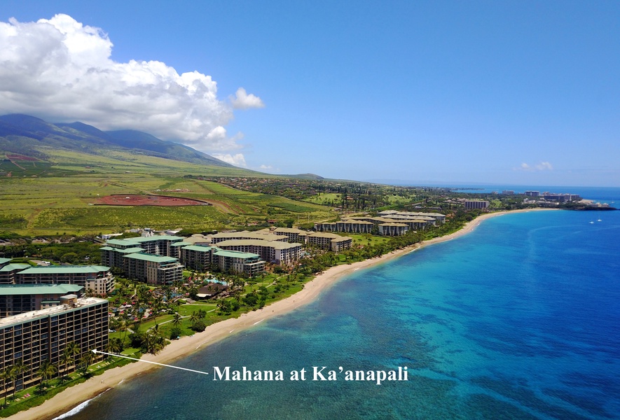 An aerial view of Mahana at Ka'anapali, showcasing its stunning beachfront location along the beautiful coastline, with lush greenery and mountains in the backdrop.