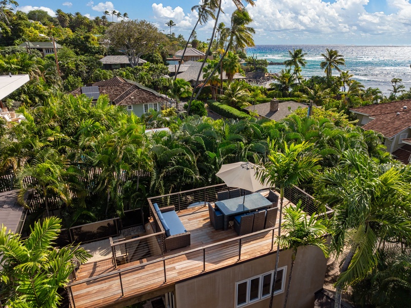 Aerial view showcases the property's tropical setting with lush palms, nearby ocean, and private rooftop terrace nestled within the coastal neighborhood.