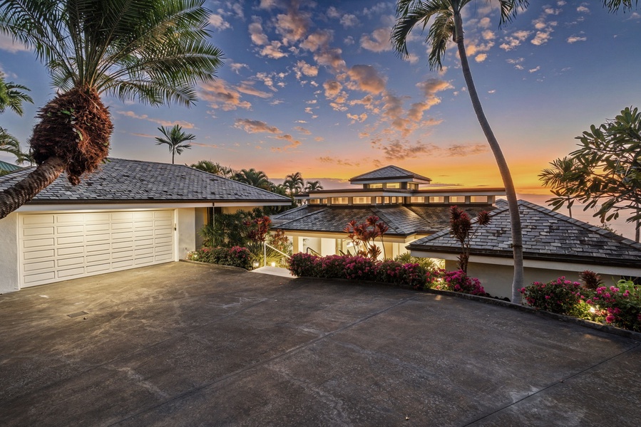Tropical paradise property featuring elegant architecture surrounded by lush palms and vibrant landscaping under dramatic sunset skies.