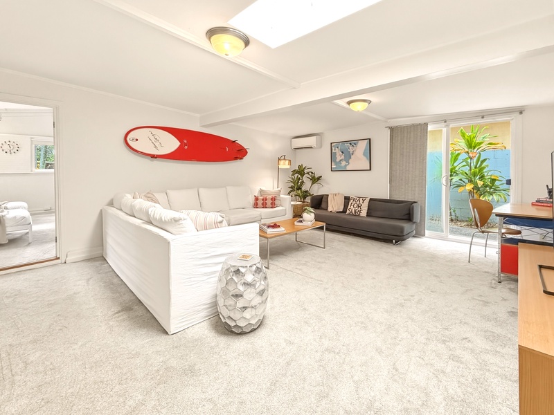 Relax in your bright, modern living space with comfortable sectional seating, stylish surfboard decor, and natural light streaming through large windows.