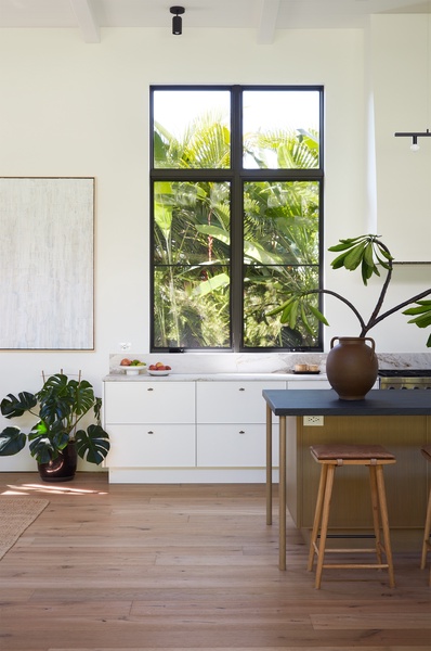 Framed by oversized windows and tropical greenery, the kitchen brings the beauty of the outdoors into everyday moments.
