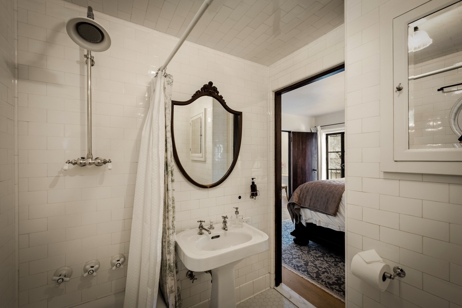 Refresh in your elegant tiled bathroom featuring a vintage-inspired mirror and rainfall shower, with classic details throughout.
