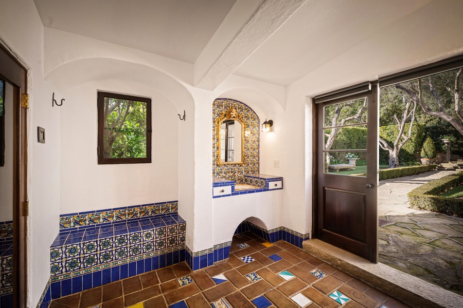 Unwind in this enchanting Spanish-style bathroom featuring handcrafted ceramic tiles, a built-in vanity, and charming garden views through large windows.