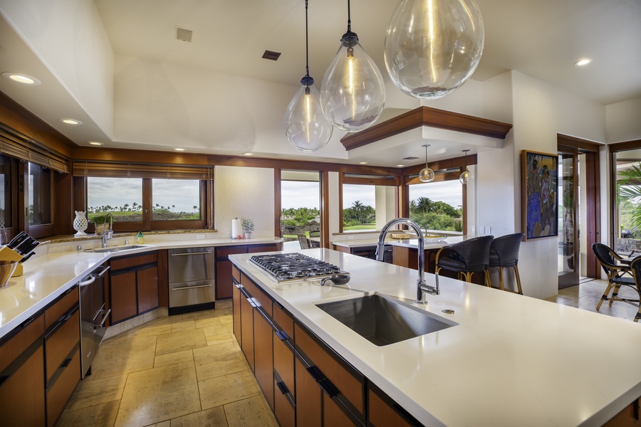 Your gourmet kitchen features gleaming countertops, professional appliances, and stunning pendant lighting, perfect for cooking while enjoying tropical views.