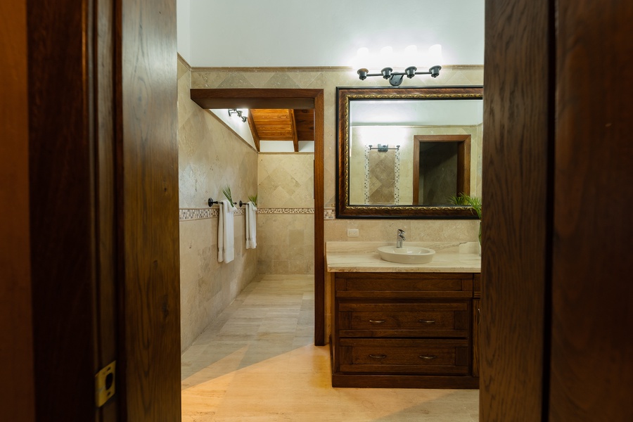 Elegant ensuite bathroom with a large mirror and wooden vanity, complemented by natural stone finishes