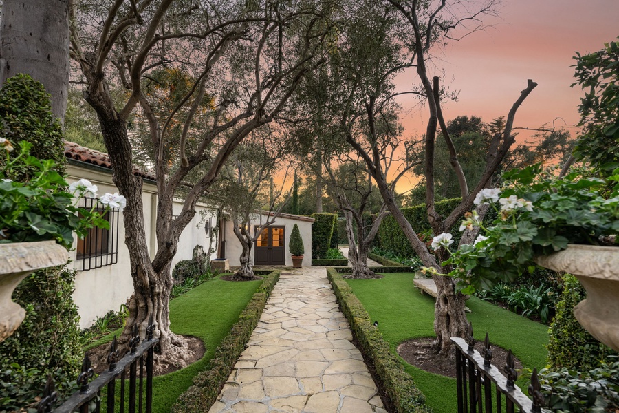 A stunning estate entrance with landscaped gardens and mature trees framing the pathway at sunset.
