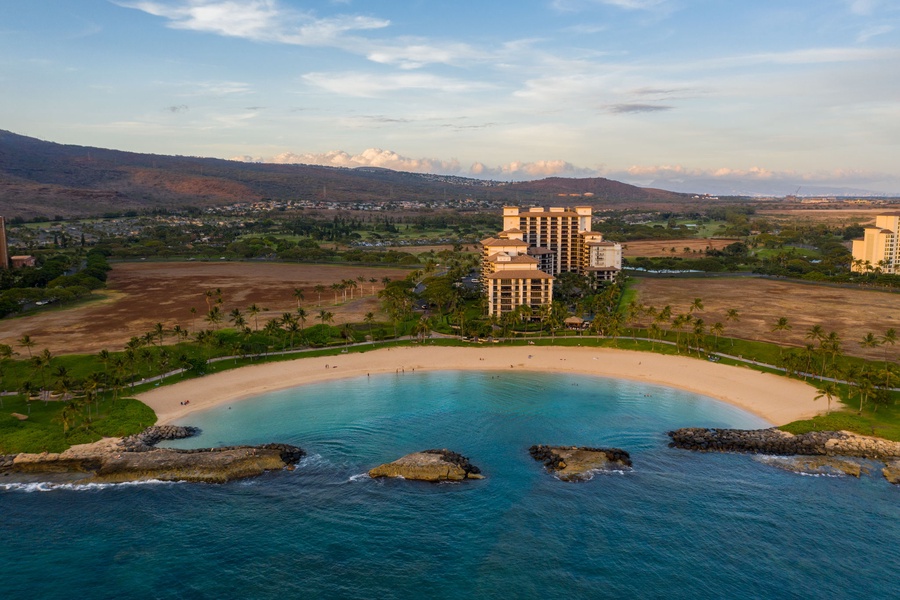 Aerial view of the oceanfront resort with pristine beach, turquoise waters, and mountain backdrop creating an idyllic Hawaiian setting.