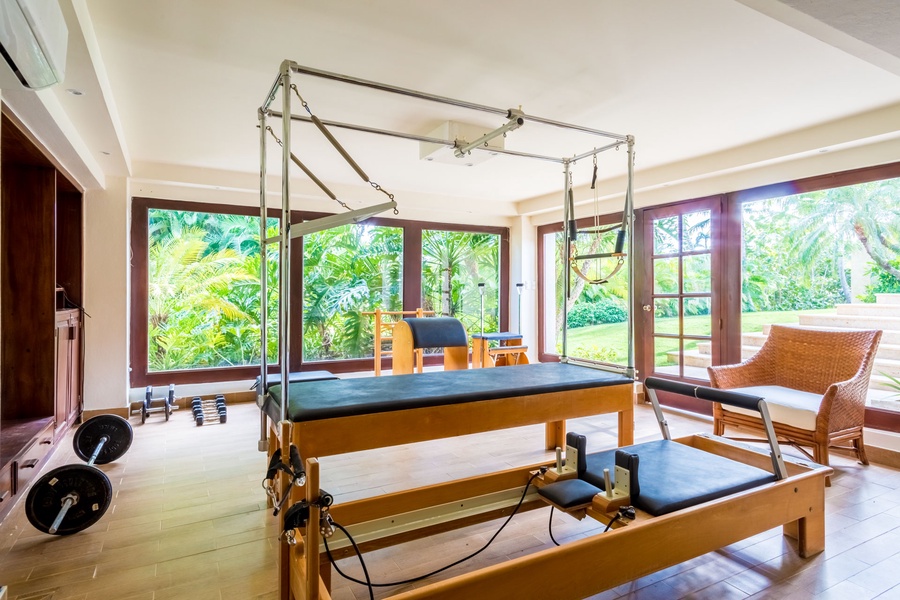 A Pilates equipment gym with floor-to-ceiling windows offering lush garden views.