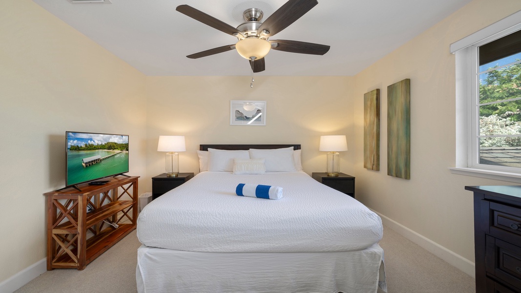 Unwind in the spacious primary suite featuring a plush king bed, ceiling fan, and soft lighting that creates the perfect setting for relaxation.