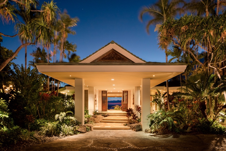 Grand entryway with tropical landscaping lit up at twilight.