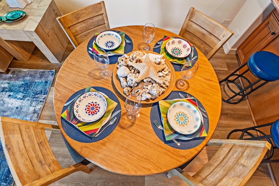 A beautifully set dining table awaits, complete with vibrant, beach-inspired dishware and a stunning seashell centerpiece