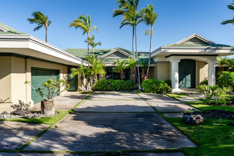 Spacious driveway leading to a beautiful tropical home, surrounded by palm trees and lush greenery.