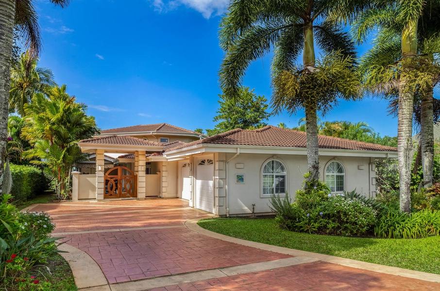 Front exterior of Ohana Kamalani, showcasing tropical landscaping and welcoming island-style architecture along a quiet Princeville street.