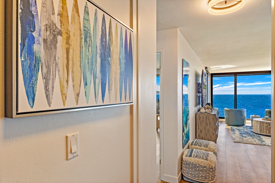 A welcoming hallway with coastal artwork leads you toward the open living space and the stunning ocean views beyond