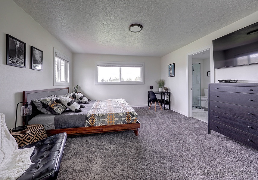 The primary bedroom boasts a king-sized bed, desk area, large closet, carpeting, and a 55” flat-screen TV