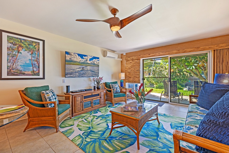 The bright and airy living room features tropical décor, comfortable seating, and large sliding doors that lead to the lanai, offering seamless indoor-outdoor living.