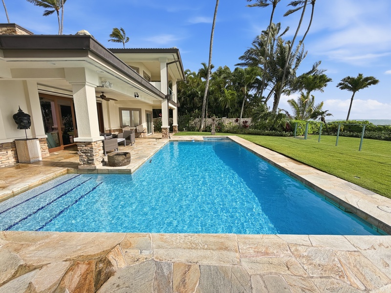 Stunning oceanfront estate with pristine pool surrounded by swaying palms and manicured lawns under tropical blue skies.