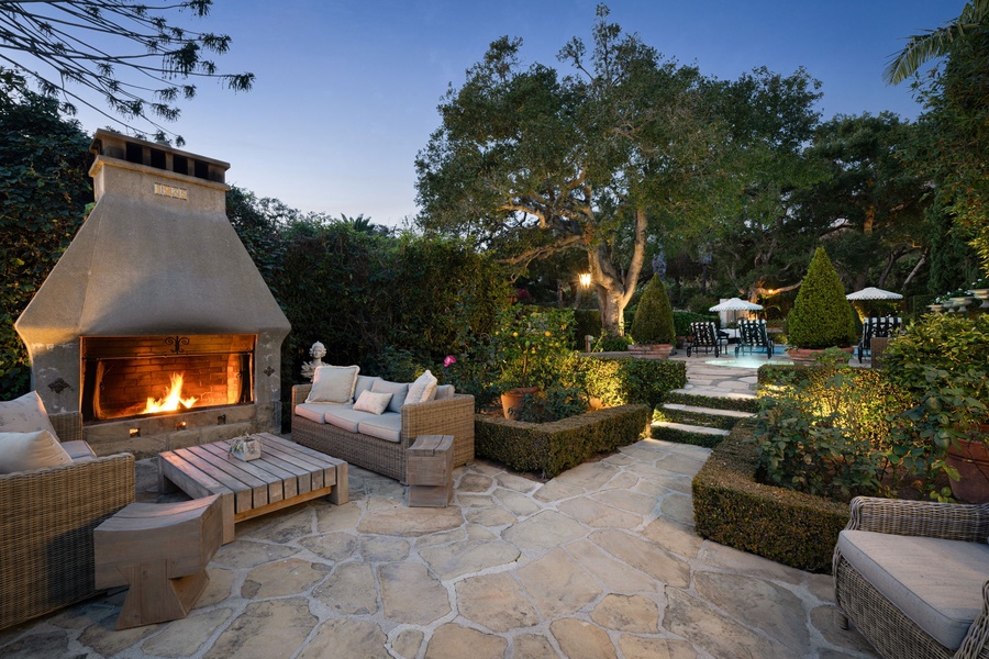Elegant outdoor fireplace creates the perfect evening ambiance in this beautifully landscaped garden setting with multiple seating areas.
