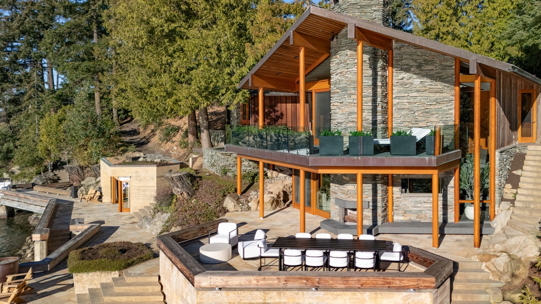 Modern lakefront retreat with stunning architecture nestled among towering trees, featuring stone and wood design elements.