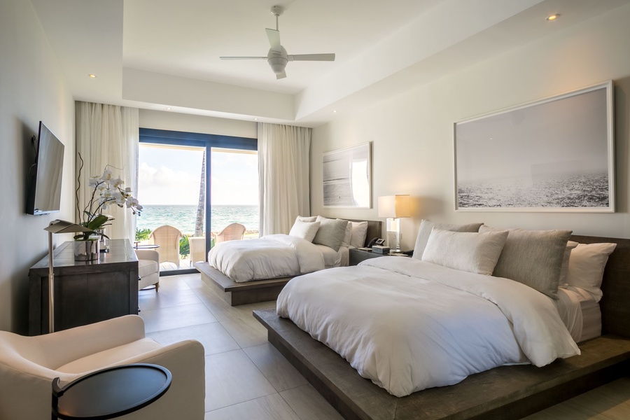 Chic and serene guest bedroom with two plush bedsand direct access to a private balcony with ocean views.
