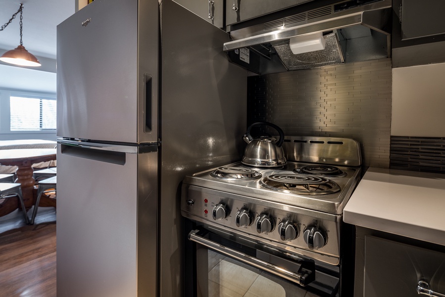 Experience culinary precision with this stainless-steel stovetop set, complemented by a modern extractor hood and adjacent spacious refrigerator.