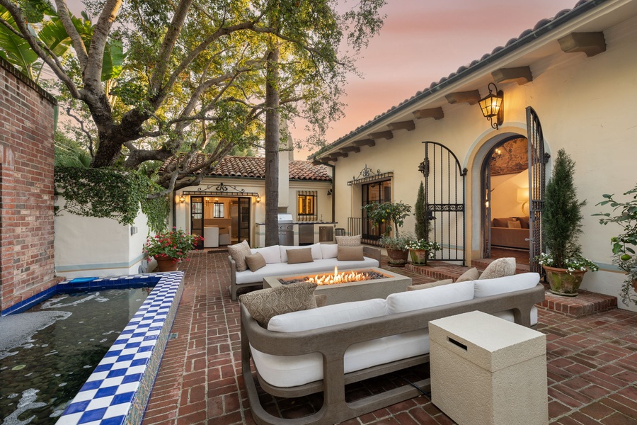 Elegant Spanish-style courtyard with fire pit, plush seating, and tranquil water feature creates your perfect evening retreat.
