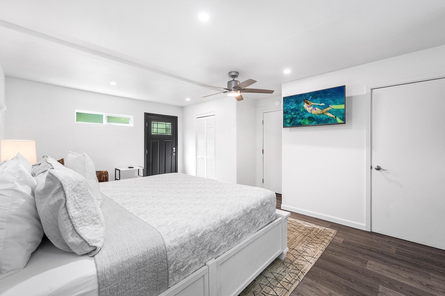 Guest bedroom with large TV, ceiling fan, and ample space to relax and recharge.
