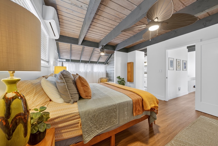 Relax in your spacious bedroom featuring exposed beam ceilings, tropical-inspired ceiling fan, and warm wood floors that create a serene island retreat atmosphere perfect for unwinding.