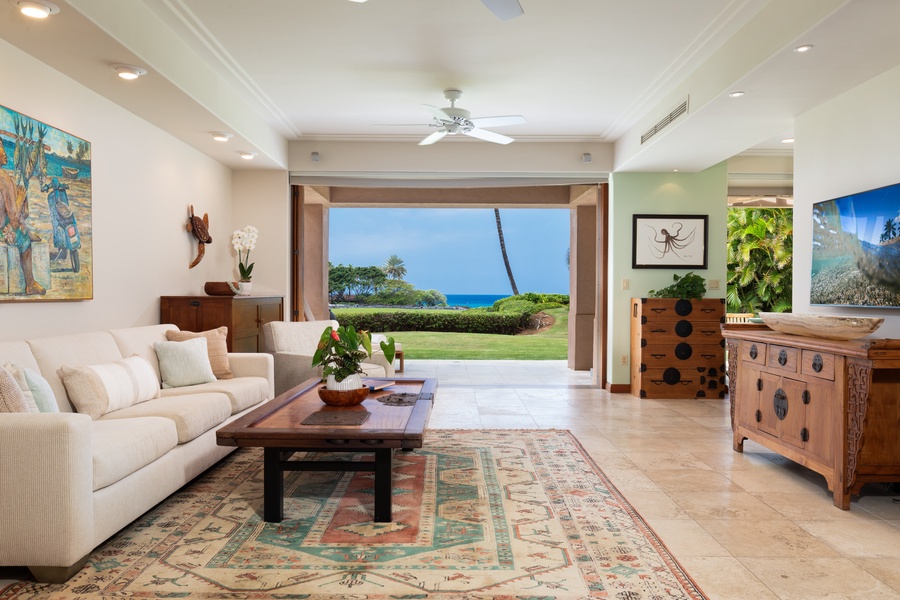 Relax in your elegant living space where floor-to-ceiling windows frame stunning ocean views, creating a seamless indoor-outdoor tropical paradise.