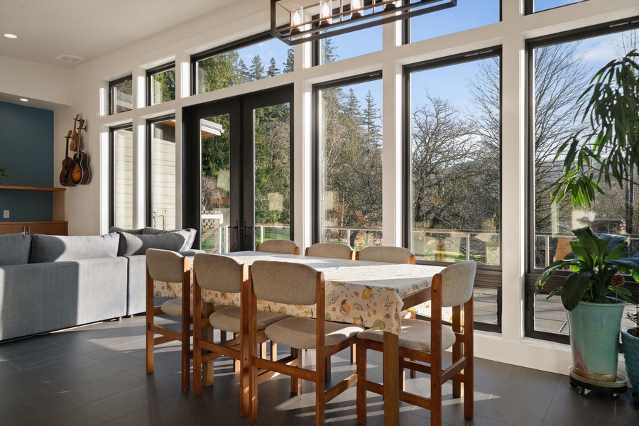 Gather around this inviting dining table where floor-to-ceiling windows frame peaceful tree views, creating the perfect backdrop for your morning coffee or evening meals.