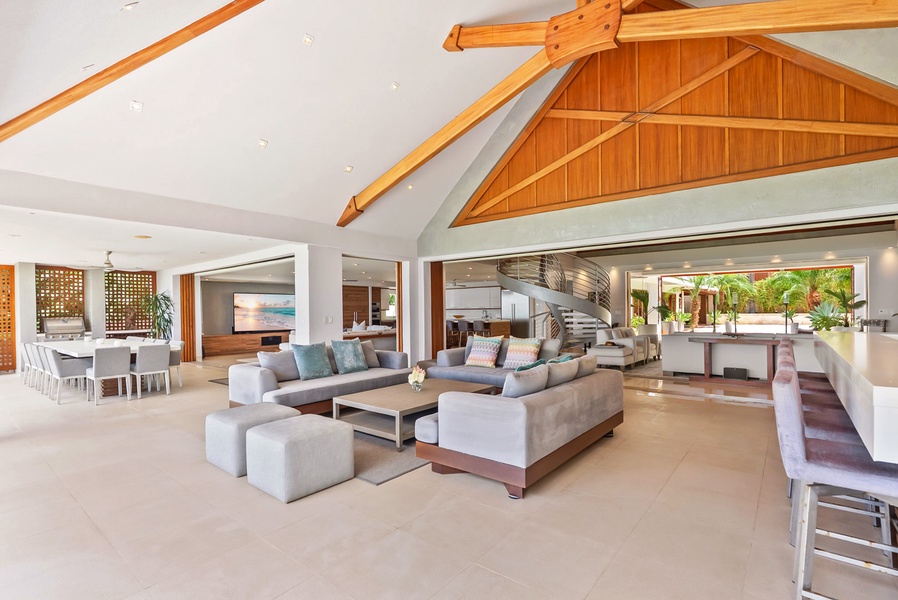 Step into your private sanctuary with soaring vaulted ceilings and warm wood beams. Relax in the spacious living area where natural light floods through floor-to-ceiling windows, opening to lush tropical gardens.