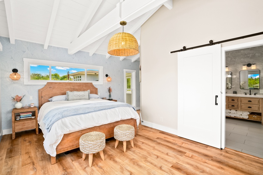 A beautifully styled bedroom featuring vaulted ceilings, natural wood flooring, and a sliding barn door for added charm.