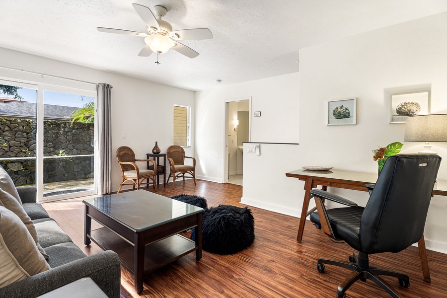 Relax in your bright office space with comfortable seating, hardwood floors, and tropical views through sliding glass doors.