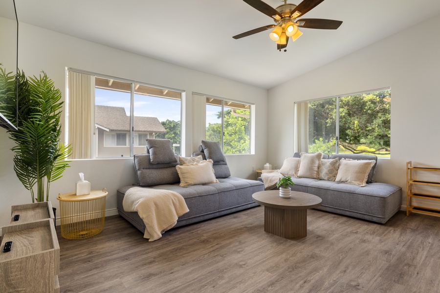 Sink into plush gray sectional seating while the ceiling fan keeps you cool in this bright, modern living space with peaceful tree views.