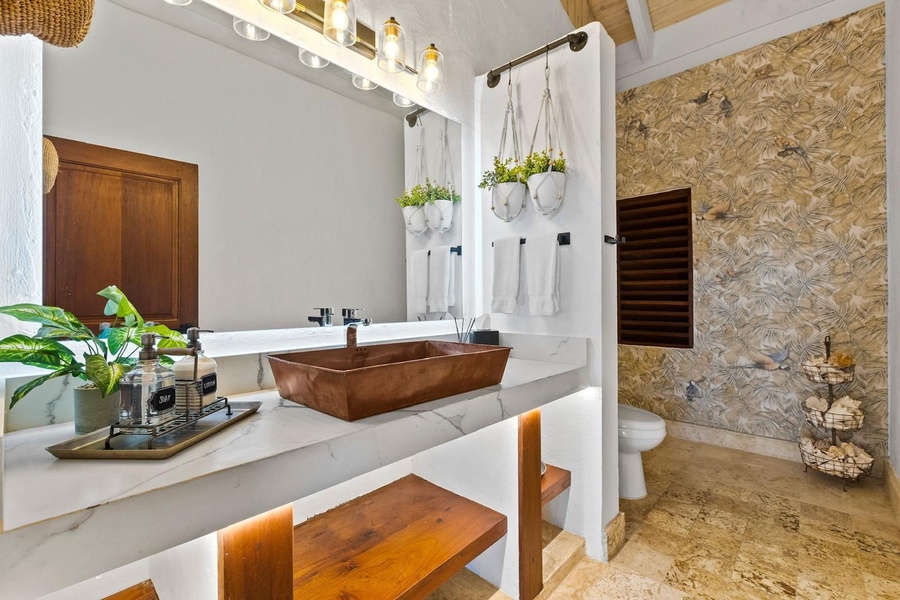 A stylish ensuite bathroom with a unique copper sink, marble countertop, and rustic wooden accents.