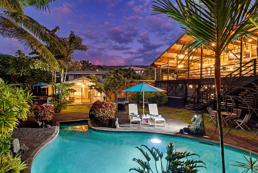 Tropical paradise awaits with illuminated swimming pool, palm trees, and modern architecture under a stunning sunset sky.