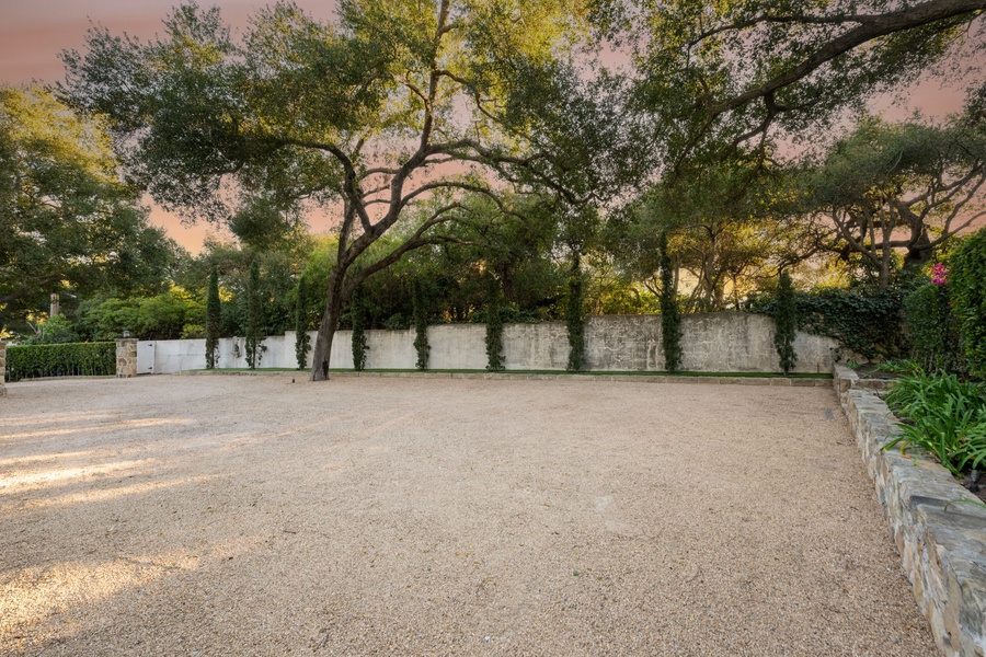Spacious gravel courtyard surrounded by mature trees and stone walls, creating a peaceful outdoor gathering space.
